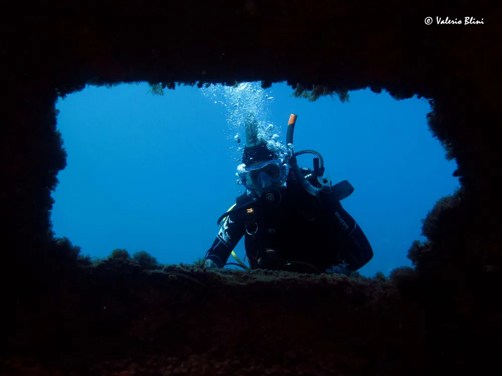 Subacqueo in immersione tra le rocce, verso l'acqua aperta
